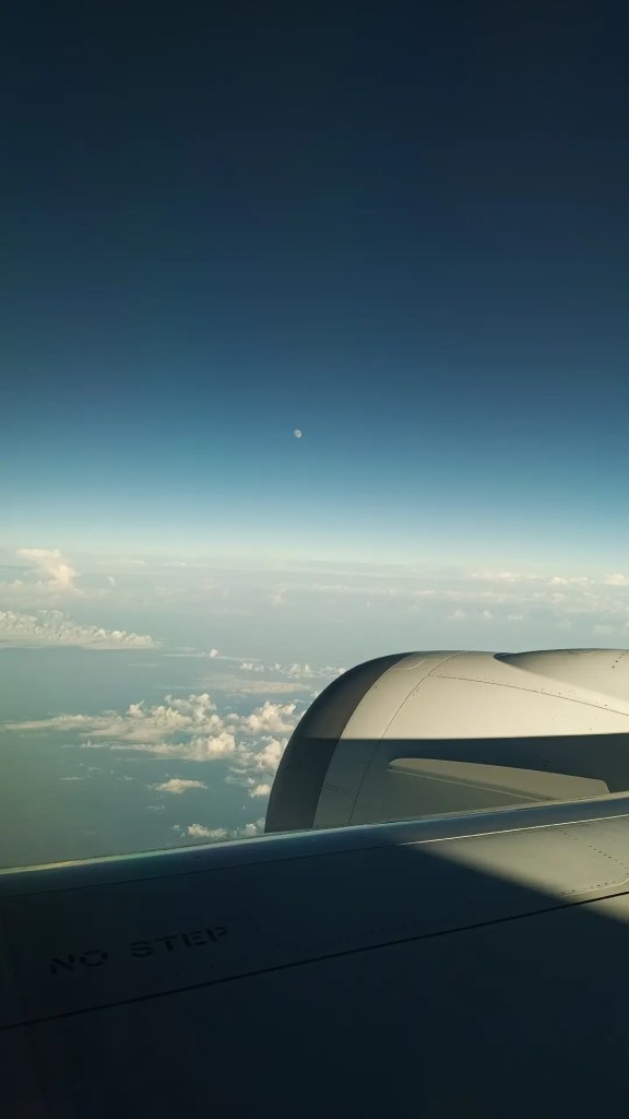 View from airplane window. Above the clouds. The moon can be seen.